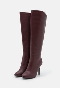 Bottes en cuir bordeaux montantes avec une forme ajustée, un bout pointu et un talon aiguille, présentant une texture lisse et un design minimaliste.