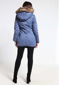 Blå parka-jacka med huva i fuskpäls, med åtdragen midja, dragkedjestängning och långa ärmar, ihop med svarta slim fit-jeans.