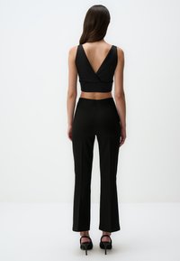 Zwarte cropped top met een V-rug, gecombineerd met zwarte aansluitende broeken. Beide stukken zijn gemaakt van gladde stof en hebben een getailleerde pasvorm. Zwarte hoge hakken.
