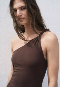 Top brown cu o singură umăr, realizat dintr-un material moale, având un detaliu cu curea răsucită. Textură netedă cu un design ajustat care pune în evidență umerii.