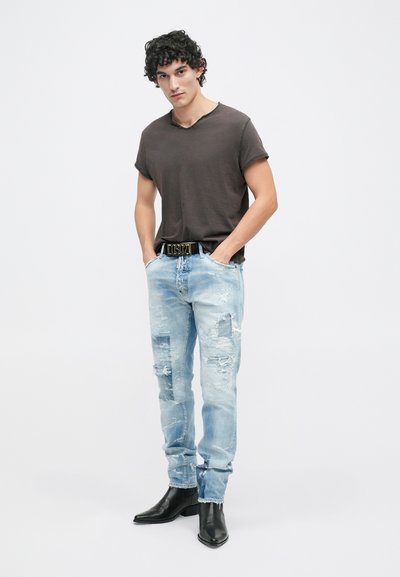 T-shirt de manga curta castanho-escuro, jeans desbotados azul-claro, cinto preto com detalhes dourados, botas pretas de bico fino. Composição de roupa casual.