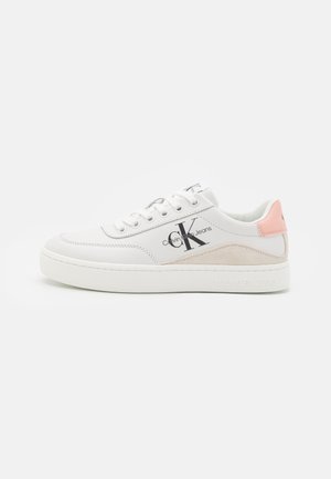Zapatilla blanca de perfil bajo Calvin Klein con cierre de cordones, detalle en ante beige, lengüeta rosa en el talón y logo negro "CK Calvin Klein Jeans" en el lateral.
