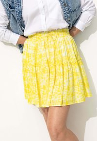 Jupe jaune à volants avec taille à cordon. Tissu léger présentant un motif tie-dye avec des nuances variées de jaune et de blanc.