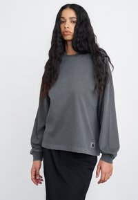 Szary longsleeve z okrągłym dekoltem i luźnym krojem. Materiał ma delikatną teksturę, z małą naszywką logo na końcu.