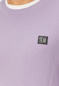 Lila strukturiertes Sweatshirt mit Rundhalsausschnitt, das auf der Vorderseite mit einem schwarzen Quadrat-Patch mit der Aufschrift "s.O" versehen ist.