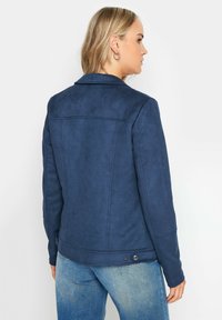Marinblå faux suede-jacka med krage, knappdetaljer och sydda detaljer. Lätt textur, skräddarsydd passform och bakvy visas.