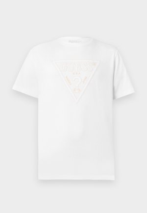 T-shirt blanc à manches courtes avec un patch logo triangle blanc en relief portant l'inscription "GUESS U.S.A. Washed Jeans" sur la poitrine.