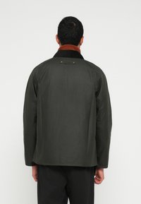 Σκούρο πράσινο αδιάβροχο μπουφάν με καφέ ριμπ κολλάρο, με ομαλή υφή και λεπτομέρειες με κουμπιά πίσω.