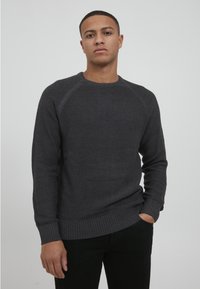 Mørkegrå strikkegenser med et teksturert mønster, rund hals og ribbestrikkede cuffs og nederkant. Ermet har raglan-design for en avslappet passform.