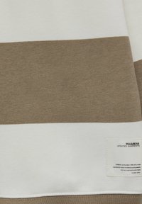 Gros plan d'un tissu avec de larges rayures horizontales beige et blanches et une étiquette blanche avec un petit texte noir dans le coin inférieur droit.