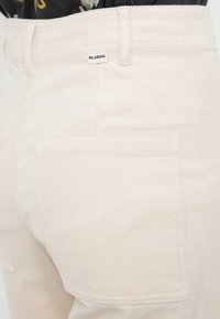 Jasnoróżowe spodnie sztruksowe z wysokim stanem, z przednimi i tylnymi kieszeniami oraz małą metką z logo Billabong na pasku.