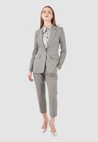 Completo grigio a righe con blazer su misura e pantaloni corti. Accompagnato da una camicia grigia chiara e scarpe con tacco metalliche. Tessuto liscio.