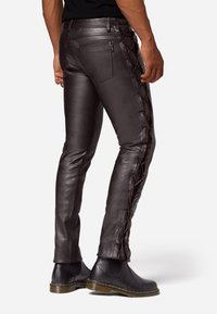 Zwarte leren broek met een strakke pasvorm, zijdelingse veterdetails in bruin en twee achterzakken, gecombineerd met zwarte enkellaarsjes.