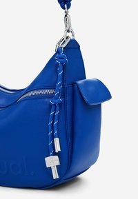 Blaues Lederhandtasche mit geschwungenem Design, silberner Hardware, einer Reißverschlusstasche und einem gemusterten Seil-Detail für den Tragegurt.