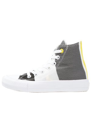 High-top sneaker med hvid sål, sorte og hvide paneler, hvide snørebånd, gul øjelet og gul stribe på hælen.