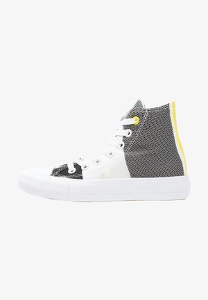 Wysoki sneaker z białą podeszwą, czarno-białymi panelami, białymi sznurówkami, żółtym oczkiem i żółtym paskiem na pięcie.