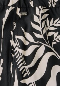 Black fabric featuring bold white leaf patterns; includes a small silver tag with text. Smooth texture with a flowing design.
