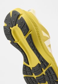 Κάτω μέρος αθλητικού παπουτσιού σε κίτρινο και μαύρο χρώμα, με υφή ελαστικού και κυρτό εργονομικό σχέδιο, εμφανιζόμενο από χαμηλή γωνία.