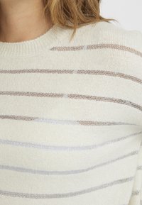 Helle Cremefarbenen Pullover mit horizontalen Streifen in sanftem Grau und metallischen Akzenten. Der Stoff wirkt weich und strukturiert und hat einen runden Ausschnitt.
