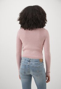 Maglione a coste rosa chiaro con maniche lunghe, design aderente, abbinato a jeans skinny blu medio con tasche posteriori e un'etichetta di marca.
