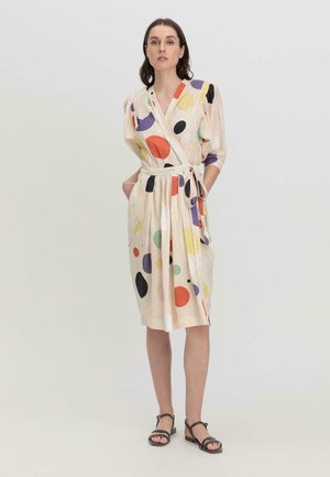 Wickelkleid aus leicht beigem Stoff, mit buntem Polka-Dot-Muster in Rot, Blau, Grün und Schwarz; beinhaltet einen Gürtel und seitliche Taschen.