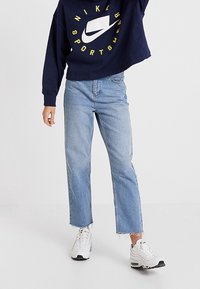 Marinblå cropped sweatshirt med gult "Nike"-logotyp, tillsammans med ljusblå raka jeans med fransade fållar och vita sneakers.