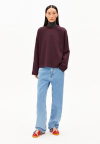 Bordeaux gestreifter Pullover, lässiger Schnitt, kombiniert mit hellblauen Straight-Leg-Jeans. Die Schuhe haben Farbakzente in Rot, Orange und Blau.
