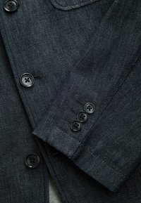 Dunkelblaue Jeansjacke mit einem Reverskragen, fünf schwarzen Knöpfen auf der Front und vier Knöpfen am Ärmel, mit einer dezenten gerippten Textur.