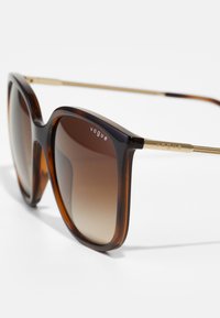 Ochelari de soare cu ramă din scoică, cu lentile pătrate supradimensionate, nuanță gradient de maro și accente metalice aurii pe tâmple, cu branding "vogue".