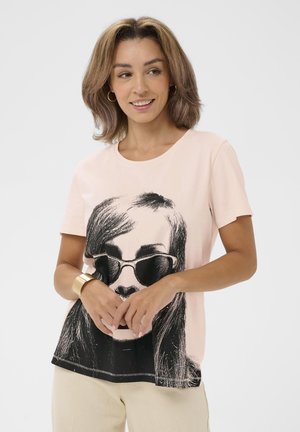Jasnoróżowy bawełniany t-shirt z czarnym nadrukiem kobiety w okularach przeciwsłonecznych, okrągłym dekoltem, krótkimi rękawami i prostym dołem.
