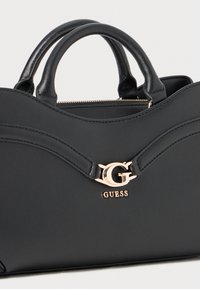Zwarte leren handtas met dubbele handvatten, voorzien van gebogen stiksels en een goudkleurig logoaccent aan de voorkant. Ritssluiting.