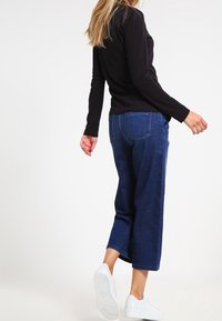 Marineblaue, cropped Jeans aus Denim-Stoff mit lockerer Passform, kombiniert mit weißen Sneakers und einem eng anliegenden schwarzen Langarmshirt.