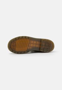 Semelle d'une chaussure avec du caoutchouc texturé à rainures profondes, une section translucide de couleur miel et un bord supérieur noir lisse.