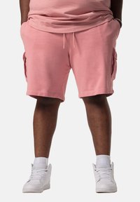 Shorts cargo en coton rose avec poches latérales, accompagnés de baskets montantes blanches. Le tissu est doux avec une coupe décontractée.