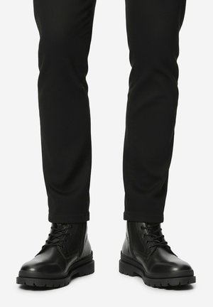Black lace-up leather boots worn with black pants, front view showing thick rubber soles and stitching details.