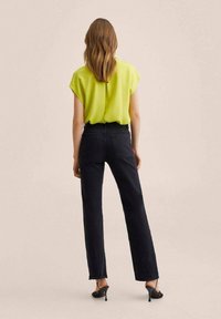 Blusa verde a maniche corte abbinata a jeans in denim scuro a vita alta e sandali neri con tacco, vista da dietro. Texture del tessuto liscia.