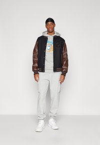 Black and brown varsity jacket with wool body and leather sleeves, gray hoodie with logo, gray sweatpants, white sneakers.