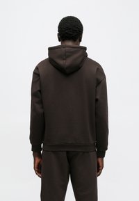 Sweatshirt castanha com capuz e um ajuste descontraído. Apresenta punhos canelados e bainha, textura suave e um bolso canguru.