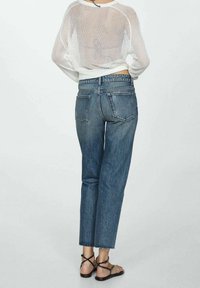 Top ligero y transparente de manga larga blanca combinado con jeans de mezclilla azul de tiro alto y pierna recta, con un corte cropped y dobladillos deshilachados.