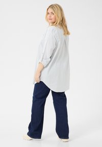 Chemise boutonnée rayée bleu clair, avec les manches longues retroussées, associée à un jean large bleu foncé et des chaussures beiges. Design simple, coupe décontractée.