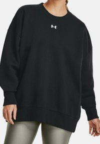 Sudadera negra de gran tamaño hecha de una mezcla de algodón, con cuello redondo ribeteado y pequeño logo blanco en el pecho. Textura suave.