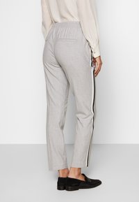 Lichtgrijze op maat gemaakte broek met een gestructureerde afwerking, elastische tailleband en zwarte zijstrepen. Beschikt over twee achterzakken en een taps toelopend been.