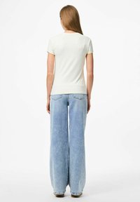 Kratkām piedurknēm ivorijas krāsa krekls, kombinējot ar gaiši zilām platām biksēm, kurām ir gluda tekstūra un smalkas šuvju detaļas aizmugurē.