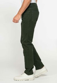 Pantaloni verdi scuri con una vestibilità slim, realizzati in cotone, dotati di tasche posteriori e dettagli di cucitura, abbinati a sneakers bianche testurizzate.