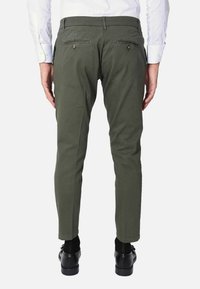 Chino verde oliva con vestibilità slim, tasche posteriori visibili con dettagli in bottone, abbinati a scarpe formali nere e una camicia bianca a maniche lunghe.