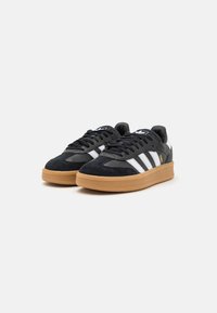Zwarte suède sneakers met witte strepen, ronde neus en rubberen gumzool. Beschikt over zwarte veters en een logo op de tong. Traditioneel ontwerp.