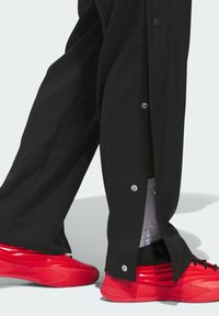 Czarne szerokie spodnie z boku zapinane na napy, zestawione z jaskrawoczerwonymi butami sportowymi i białymi skarpetkami do kostek. Wykonane z gładkiego materiału o prostych liniach.