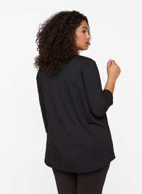 Schwarzes Langarmoberteil mit abgerundetem Saum und glattem Stoff, von hinten gesehen, mit klassischem Schnitt und minimalistischem Design.