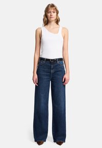 Vit linne i kombination med mörkblå vida jeans. Jeansen har klassisk femficksdesign och ett svart bälte. Snyggt tyg med slät yta och rena linjer.