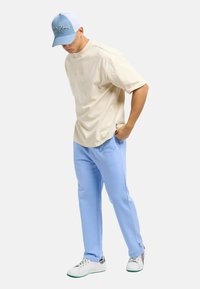 Beige short-sleeve t-shirt, light blue sweatpants with logo embroidery, and white sneakers with colorful accents; casual outfit.